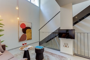 A modern interior with a staircase, a flat-screen TV, and abstract art.