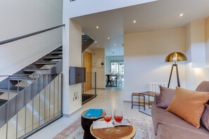 A modern living room with a staircase, a dining area, and a sofa with cushions.