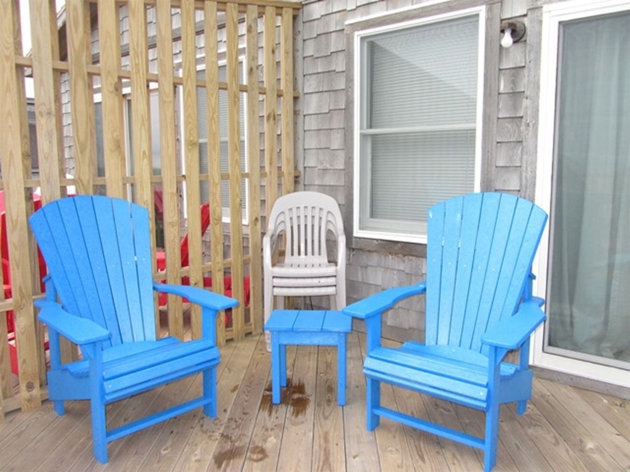 Une terrasse en bois avec deux chaises Adirondack bleues et une chaise en plastique blanche.