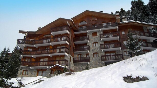 Un hotel de varios pisos con balcones y muros de piedra, rodeado de nieve.
