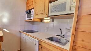 Cocina compacta con armarios de madera, microondas, lavavajillas y un lavamanos.