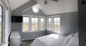 A bedroom with a large bed, a TV mounted on the wall, and multiple windows offering a view of the outdoors. - Modern house at Wells Beach - Available Winter Rentals Off Season-reduce rate. (Wells)