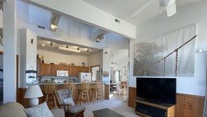 A living room with a sofa, chairs, a TV, and a kitchen in the background. - The Baited Hook a great vacation destination for the family! (Frisco)