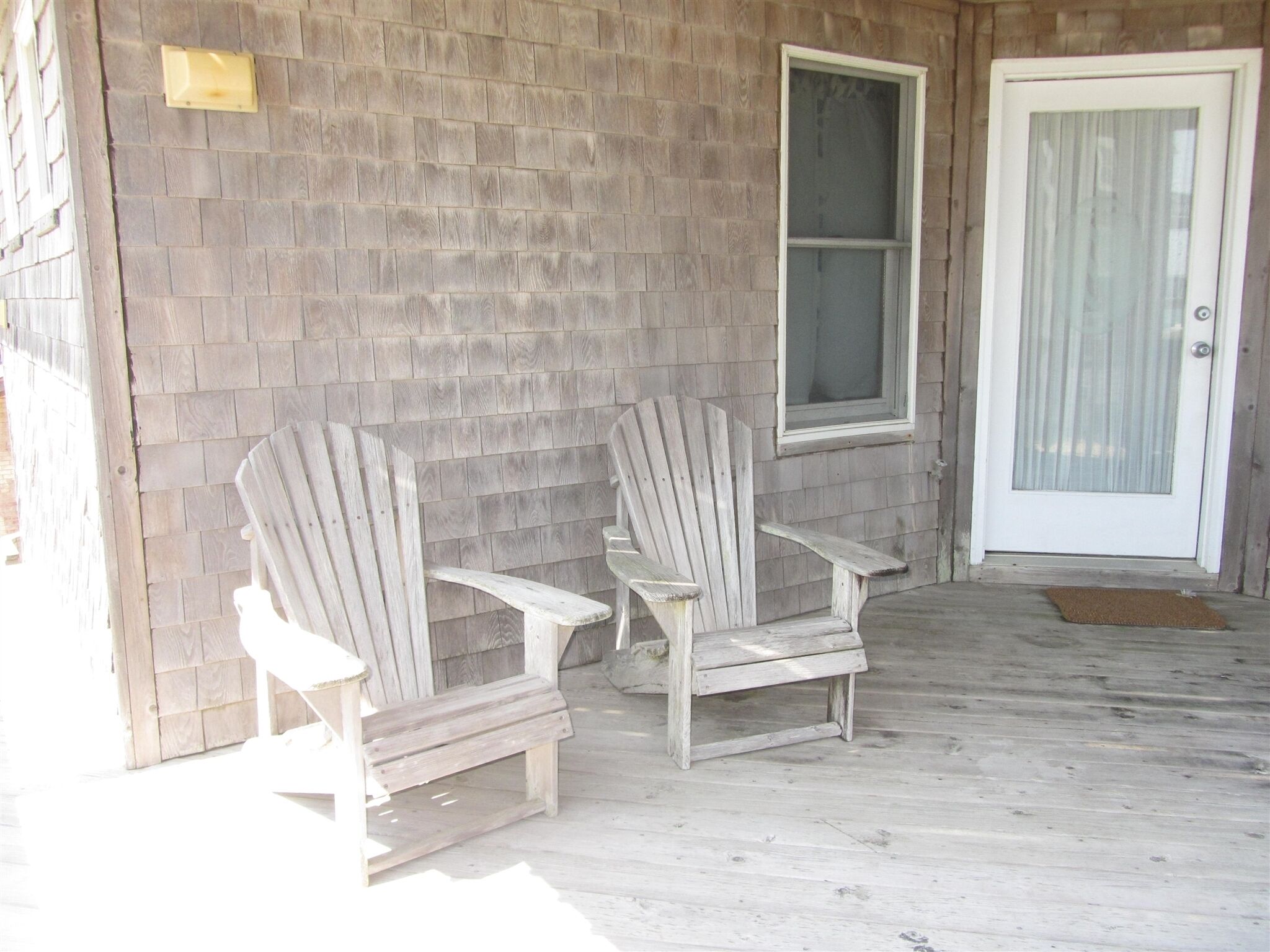 A porch with two Adirondack chairs, a wooden door, and a window.