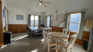 A room with a dining table and chairs, a ceiling fan, windows with curtains, and a wall-mounted lamp. - The Baited Hook a great vacation destination for the family! (Frisco)