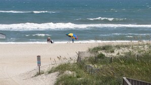 A beach with a wooden fence, a sign, and a person with a colorful umbrella. - The Baited Hook a great vacation destination for the family! (Frisco)