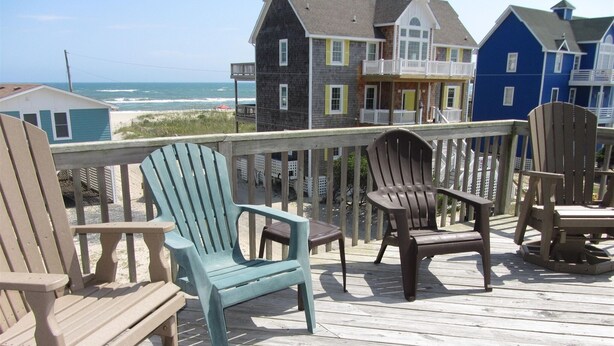 A wooden deck with Adirondack chairs and a view of a beach and houses. - The Baited Hook a great vacation destination for the family! (Frisco)