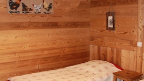 Ein Zimmer in einer Holzhütte mit einem Bett, einem kleinen Tisch und einem an der Wand hängenden Bild von Hühnern.