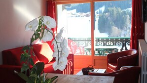 Ein gemütliches Zimmer mit einem roten Sofa, einem Tisch mit einer Karte und Blick auf eine verschneite Landschaft durch ein großes Fenster.