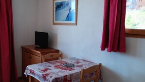A room with a table, a chair, a TV on a cabinet, a framed picture on the wall, and a window with curtains. - 26m² Studio for 2 People PMR in Puy-Saint-Vincent (Puy-Saint-Vincent)