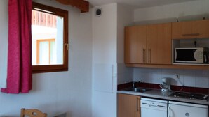 A compact kitchen with wooden cabinets, a microwave, a sink, and a dishwasher. - 26m² Studio for 2 People PMR in Puy-Saint-Vincent (Puy-Saint-Vincent)