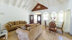 A spacious living room with a high ceiling, a sofa set, a dining table with chairs, and a door leading to another room.