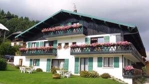 A two-story building with balconies adorned with flowers, a green roof, and a well-maintained lawn. - Lys Martagon - Chalet Fleur des Alpes (LES GETS)