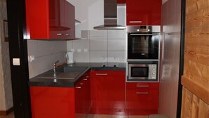 A compact kitchen with red cabinetry, a stainless steel sink, and two built-in ovens. - Lys Martagon - Chalet Fleur des Alpes (LES GETS)