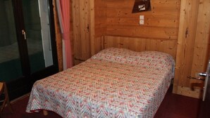 A small, wooden room with a bed, a door, and a small shelf with a photo. - Lys Martagon - Chalet Fleur des Alpes (LES GETS)