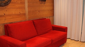 A red sofa in a room with wooden walls and a white curtain. - Lys Martagon - Chalet Fleur des Alpes (LES GETS)