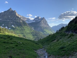 A mountainous landscape with a stream, dense forest, and rocky peaks. - Upscale lodging duplex minutes from Glacier NP (Coram)