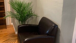 A corner room with a leather armchair, a large potted plant, a framed picture on the wall, and a thermostat. - Upscale lodging duplex minutes from Glacier NP (Coram)