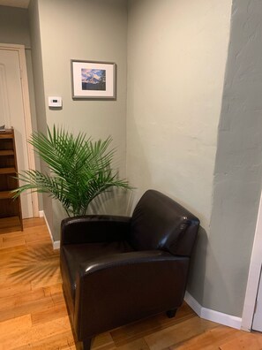 A corner room with a leather armchair, a large potted plant, a framed picture on the wall, and a thermostat. - Upscale lodging duplex minutes from Glacier NP (Coram)