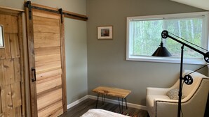A room with a wooden sliding door, a small wooden table, a chair, a floor lamp, and a window with blinds. - Upscale lodging duplex minutes from Glacier NP (Coram)