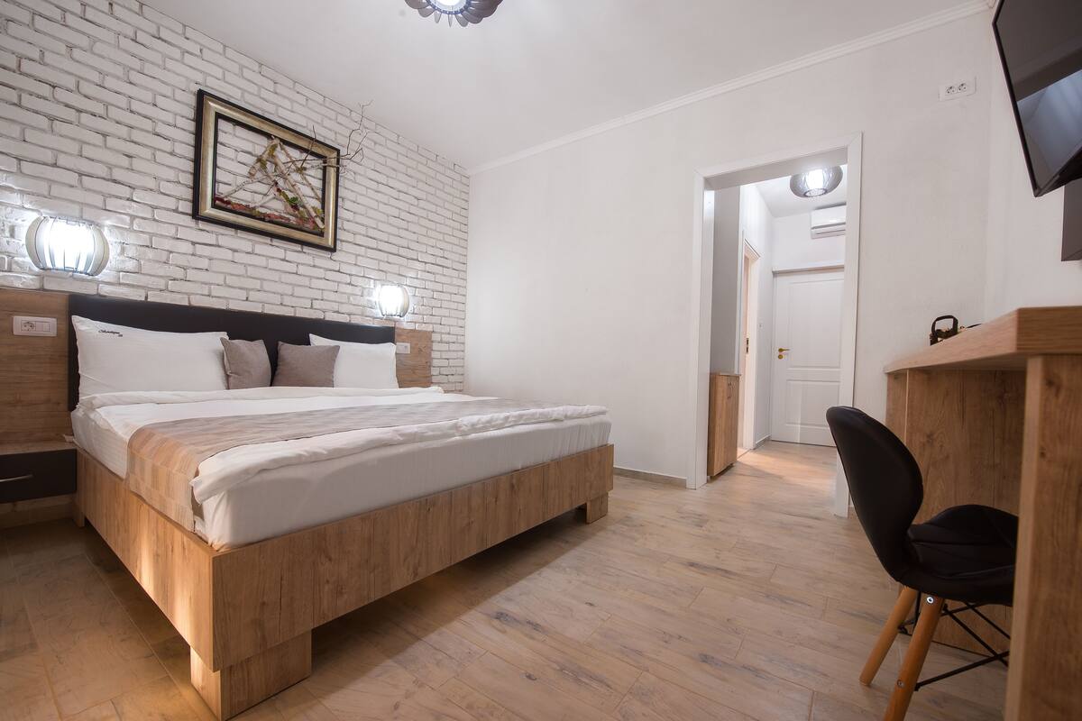 A modern bedroom with a wooden bed, white brick wall, and a desk area.