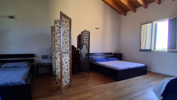A room with two beds, a wooden ceiling, a window with curtains, and a wooden floor.