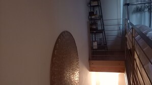 A staircase with a wooden handrail and a metal railing, leading to a landing with a metal shelf unit and a wall-mounted decorative piece.