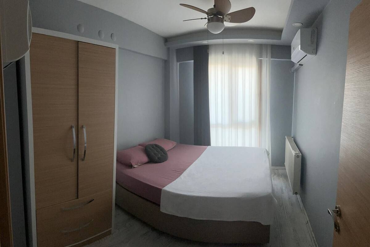Ein Schlafzimmer mit Bett, Kleiderschrank, Deckenventilator und einem Fenster mit Vorhängen.