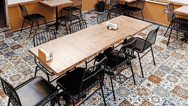 Un espace repas comprenant plusieurs tables et chaises, un sol à motifs et un mur orné d’une grille et d’objets décoratifs.