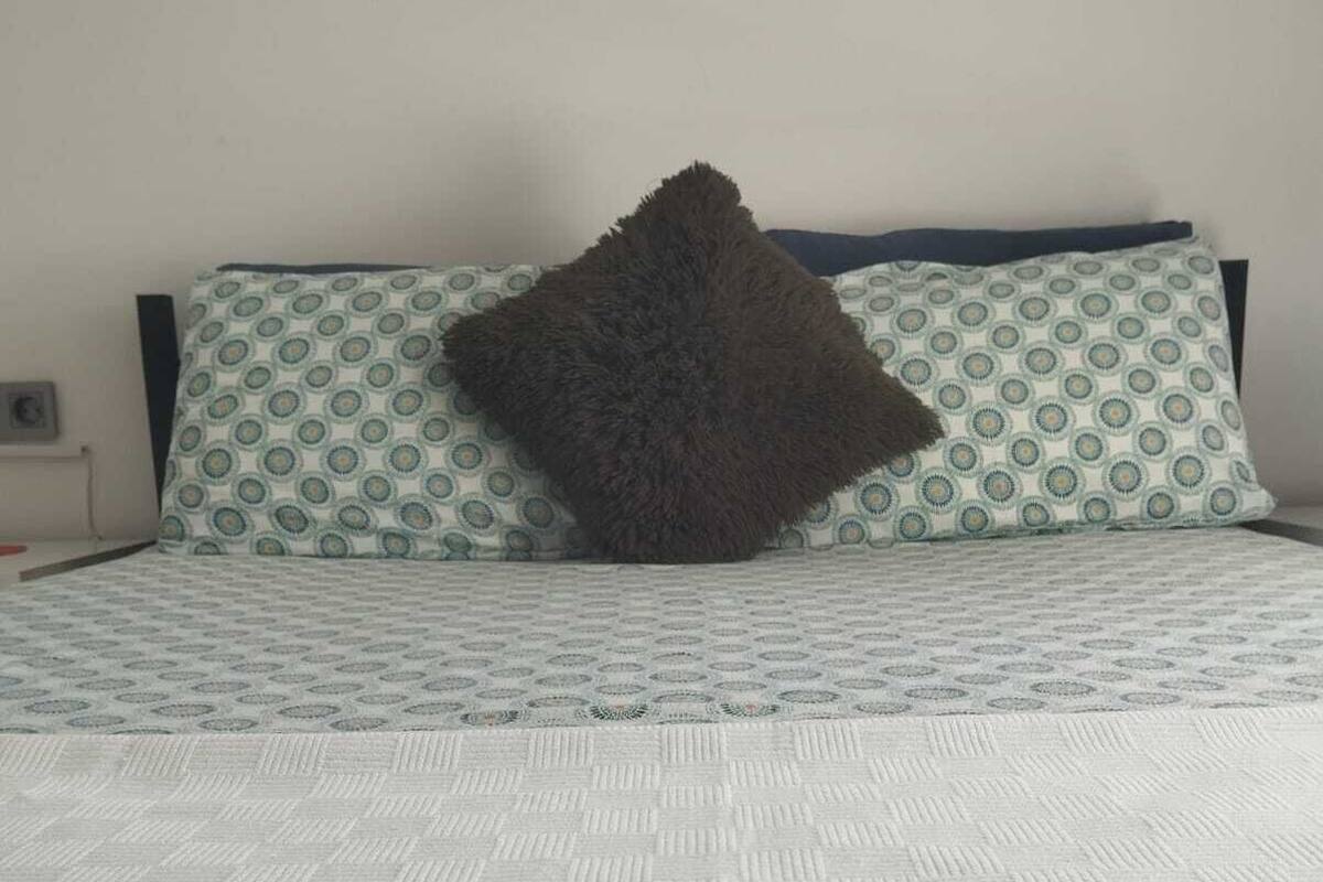 Ein Bett mit weißer Bettdecke und einem Kissen mit geometrischem Muster.