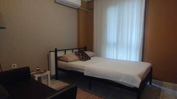 Ett hotellrum med en säng, ett litet bord, en stol och en luftkonditioneringsanläggning.