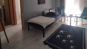 Une chambre à coucher avec un lit, un ventilateur de plafond, un tableau, une fenêtre avec des rideaux et une petite table avec des chaises.
