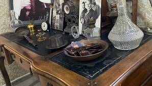 Un bureau en bois d’époque, orné d’une photographie encadrée, d’une horloge, d’une lampe en laiton et d’une carafe en cristal.