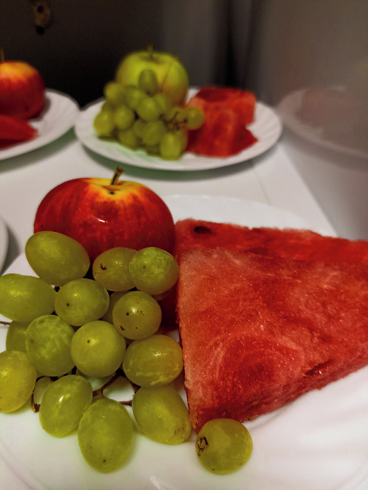 A table with plates of fruits including apples, grapes, and watermelon.