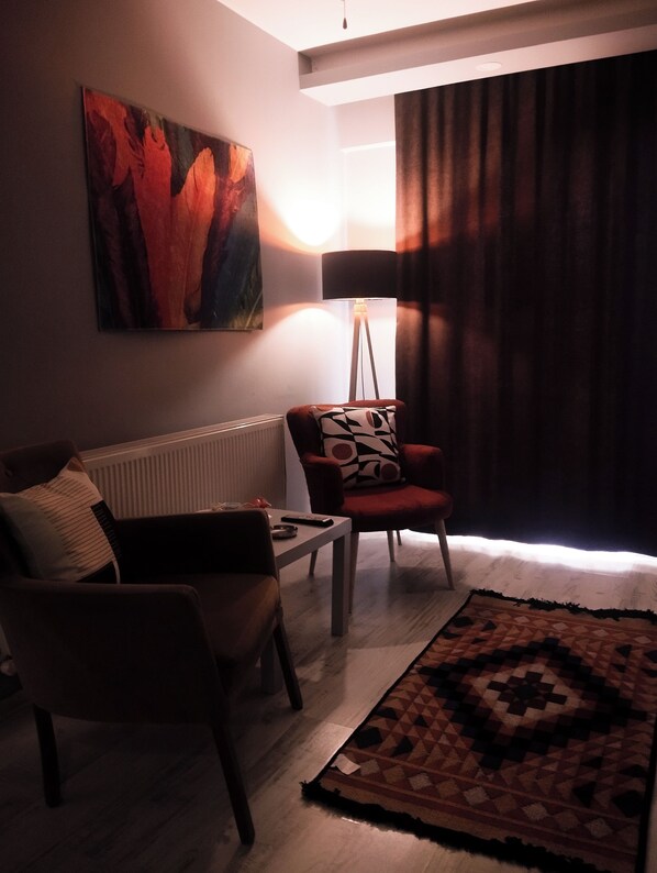 Een woonkamer met een bank, fauteuil, vloerlamp en een schilderij aan de muur.