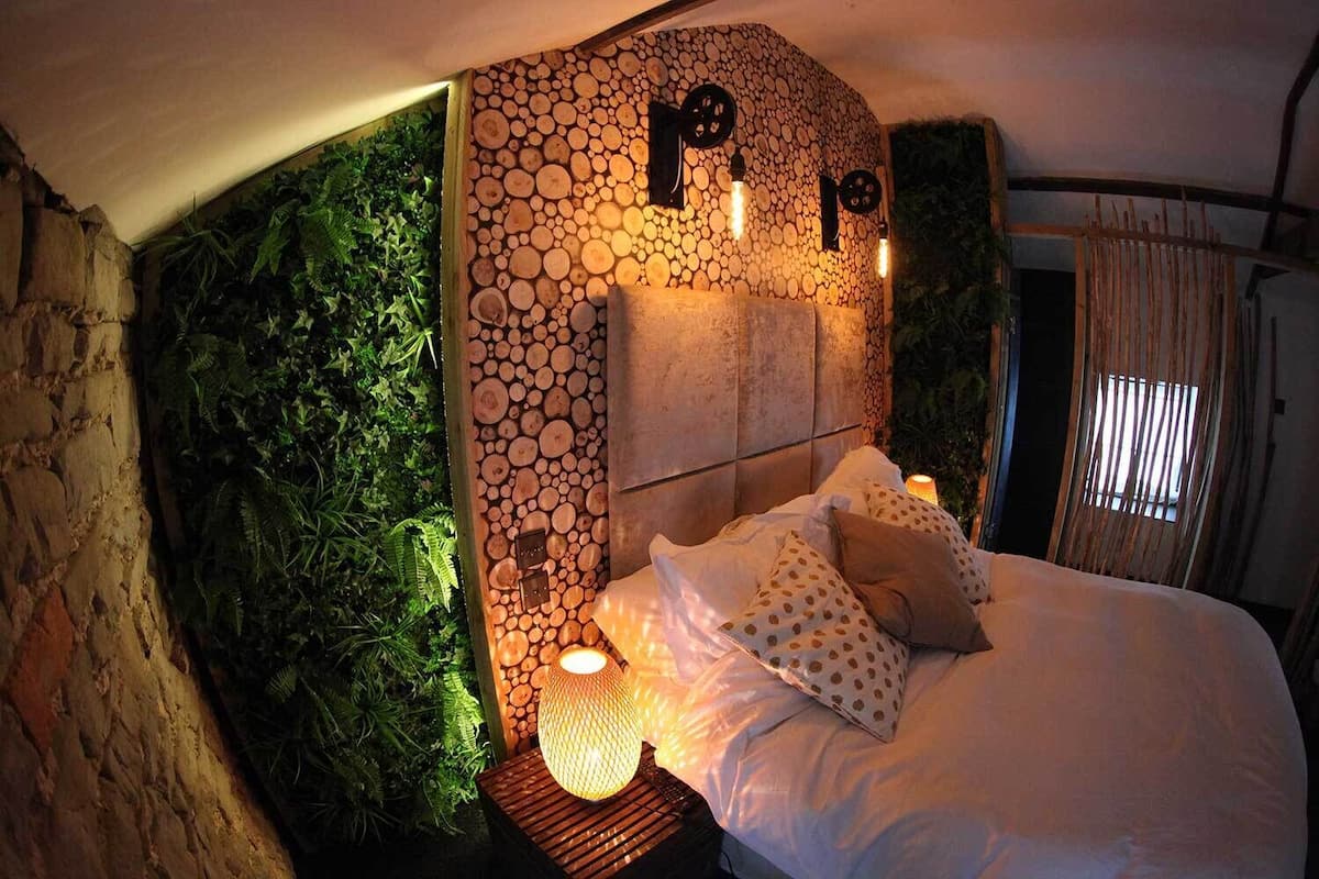 Ein Schlafzimmer mit Steinwand, einem Bett mit weißer Bettwäsche und Punkte-Kissen sowie einem kleinen Tisch mit Lampe.