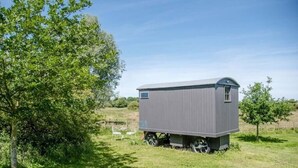 Um pequeno edifício térreo com telhado plano e uma pequena janela, localizado em um campo gramado com árvores ao fundo.