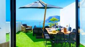 Eine Terrasse mit Esstisch, Stühlen und einem großen Sonnenschirm.
