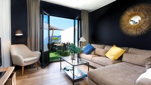 Ein modernes Wohnzimmer mit einer Couch, einem Sessel und einem Couchtisch. Ein großes Fenster bietet Blick auf einen Essbereich im Freien.