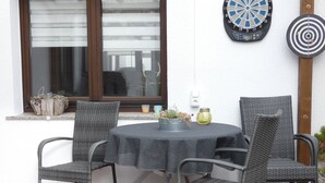 Um pátio com uma mesa redonda e quatro cadeiras, um alvo de dardos e uma janela com persianas.