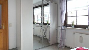 Quarto com cama, guarda-roupa, radiador e janela com cortinas.