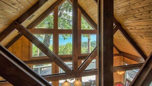 A wooden interior with large windows offering a view of a lake and trees.