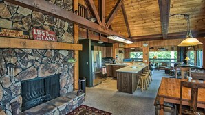 A rustic cabin interior with a stone fireplace, wooden beams, a kitchen area, and a dining space.