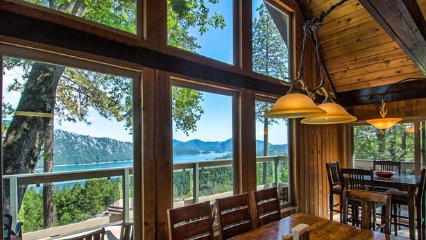 A wooden dining area with large windows offering a view of mountains and a lake.