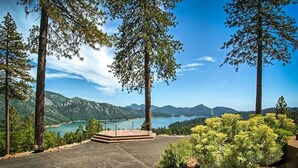 A paved viewing platform with steps, surrounded by tall trees and a clear view of a lake and mountains.
