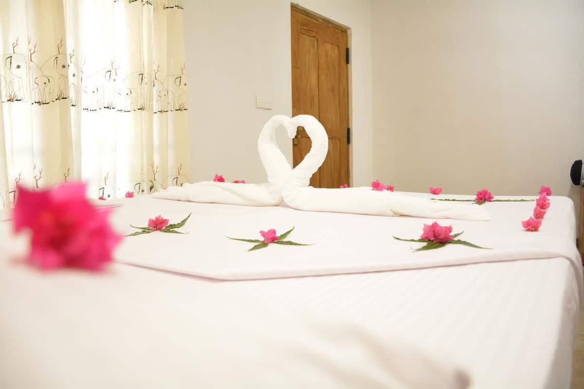 A neatly made bed with a heart-shaped towel and pink flowers.