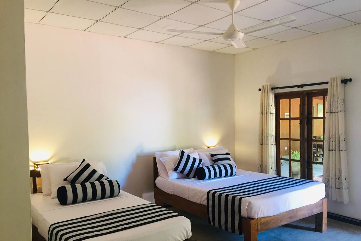 A room with two beds, each with striped bedding and pillows, a ceiling fan, and a window with curtains.