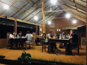 An outdoor dining area with tables and chairs, under a metal roof structure.