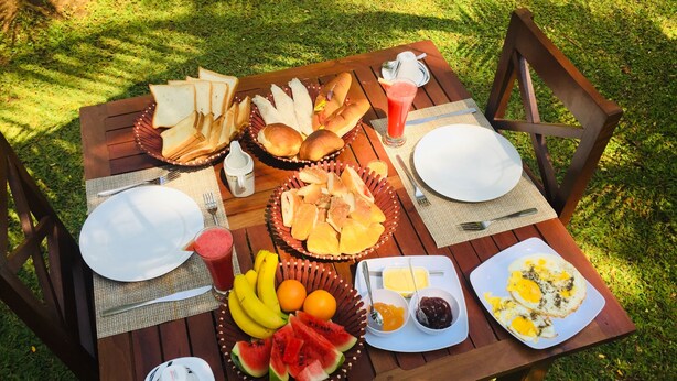 A wooden picnic table set outdoors with various food items including bread, fruits, and a drink. - Jaye Eco Lodge (Habarana)