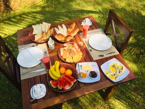 A wooden picnic table set outdoors with various food items including bread, fruits, and a drink. - Jaye Eco Lodge (Habarana)
